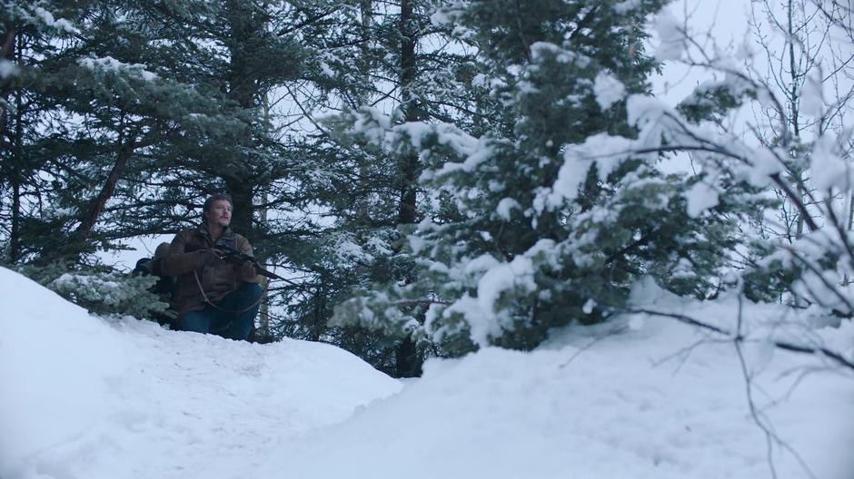 Joel looks around from the trees beside the river after firing off a shot.