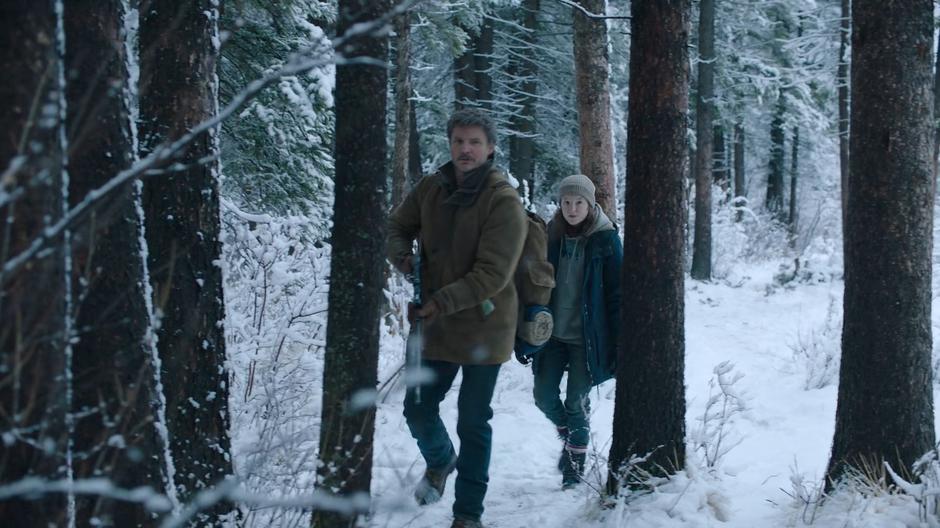 Joel and Ellie approach the bridge through the trees.