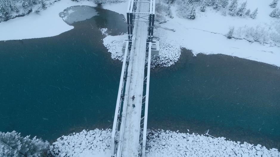 Joel and Ellie walk across the snow-covered bridge.