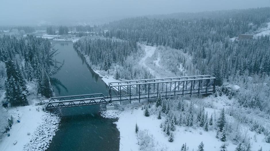 Joel and Ellie cross the bridge as snow falls around them.