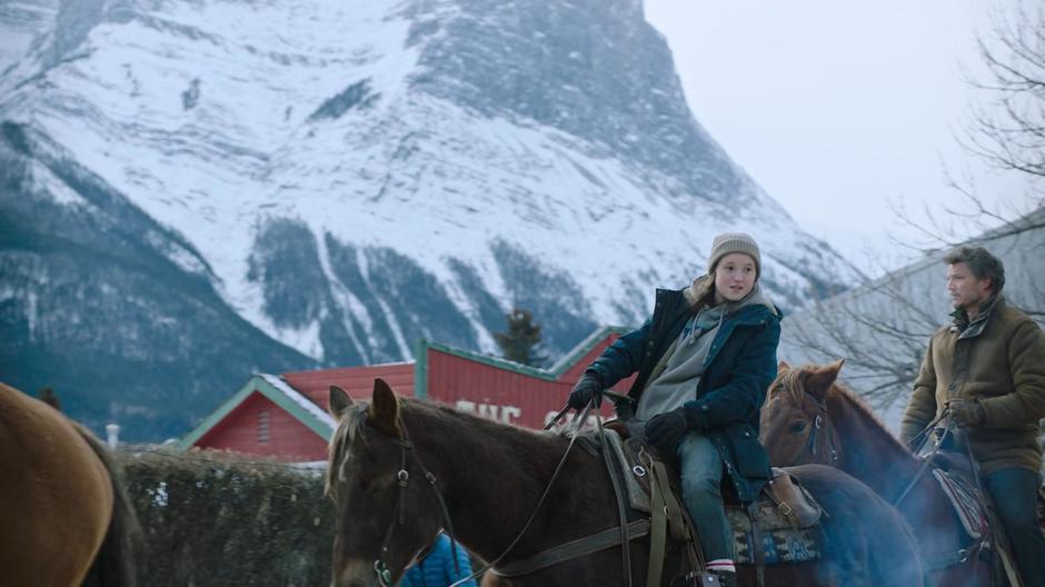 Ellie looks around as she rides into town with Joel.