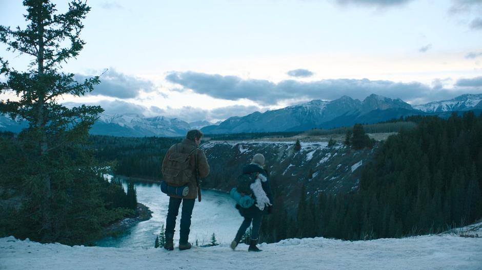 Joel and Ellie stand at the edge of the bluff looking down at the river as dusk arrives.