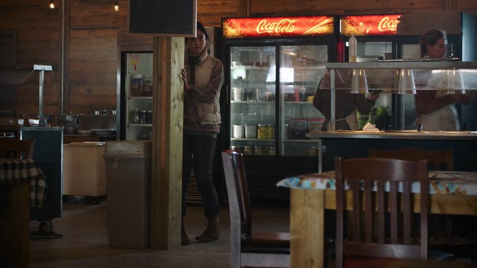 A girl stares at Ellie from behind a pillar across the room.