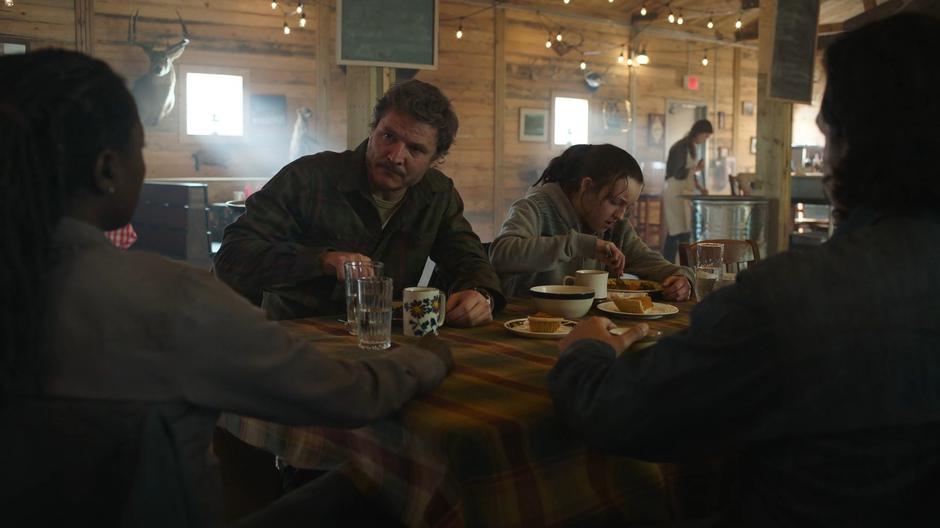 Joel looks over at Maria while Ellie continues scarfing down her food.