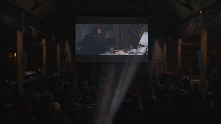 A movie is projected onto a screen in front of the crowded room.