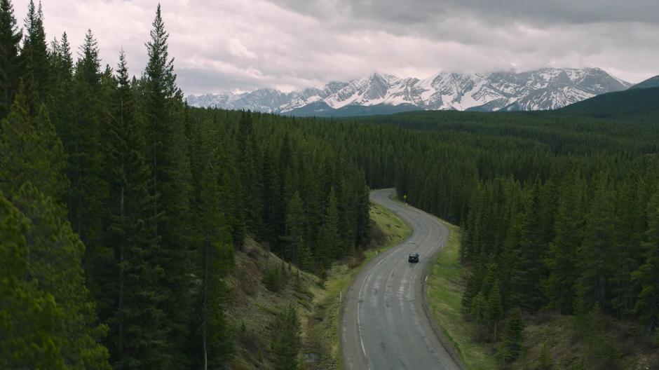 Joel and Ellie drive around the curves in the road through the forest.