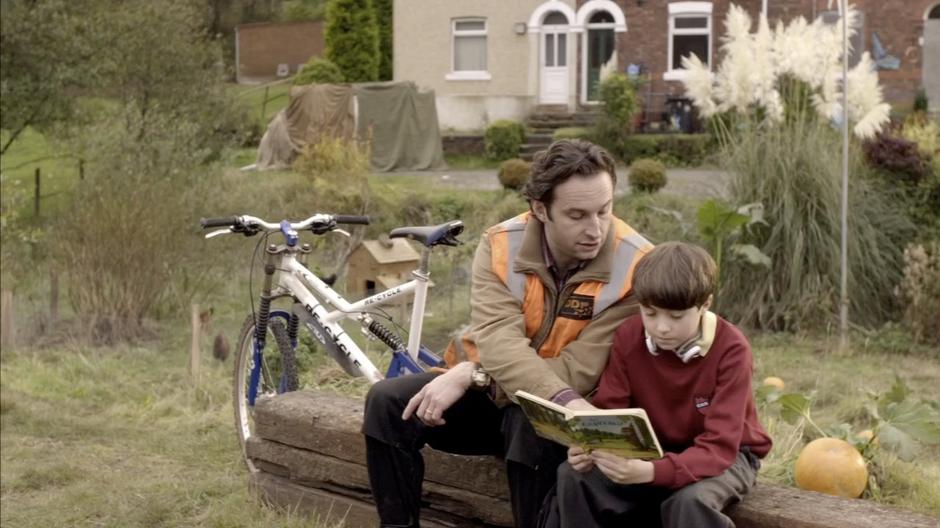 Mo helps his son Eliot read a book in front of their house.