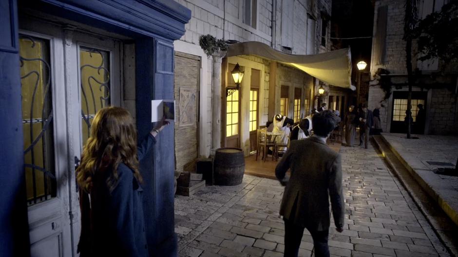 The Doctor walks up to the cafe while Amy compare it to the painting in her book.