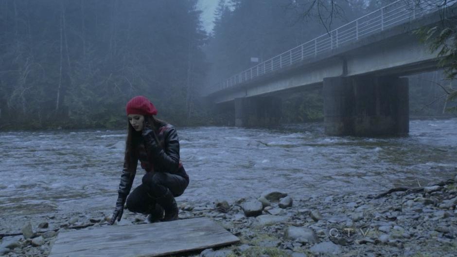 Ruby examines the ground next to the bridge while talking to Emma on the phone.