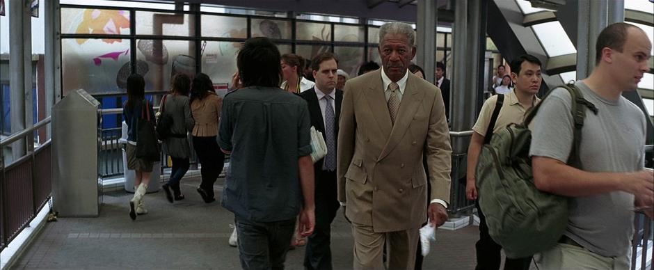 Lucius Fox approaches Bruce Wayne on the pedestrian overpass.