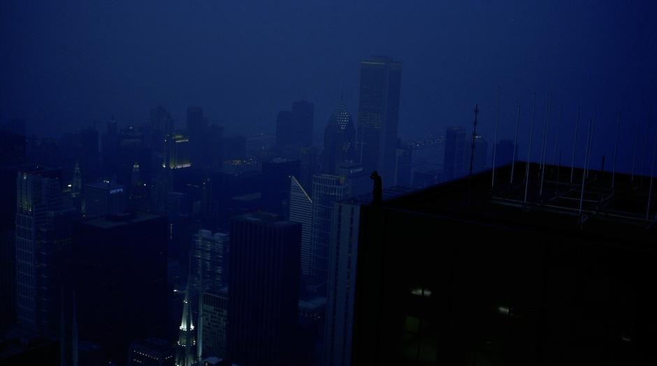 Batman stands atop a skyscraper while listening to radio signals.