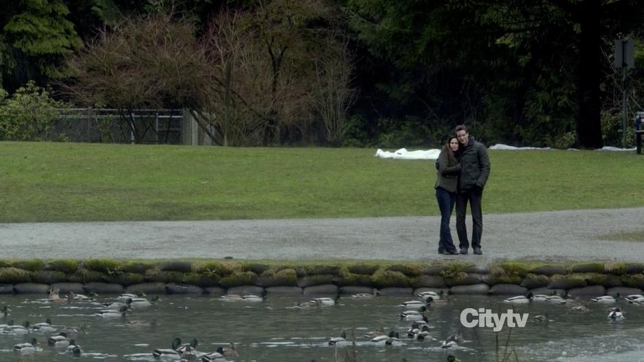 A couple hugs while watching ducks on the lake.