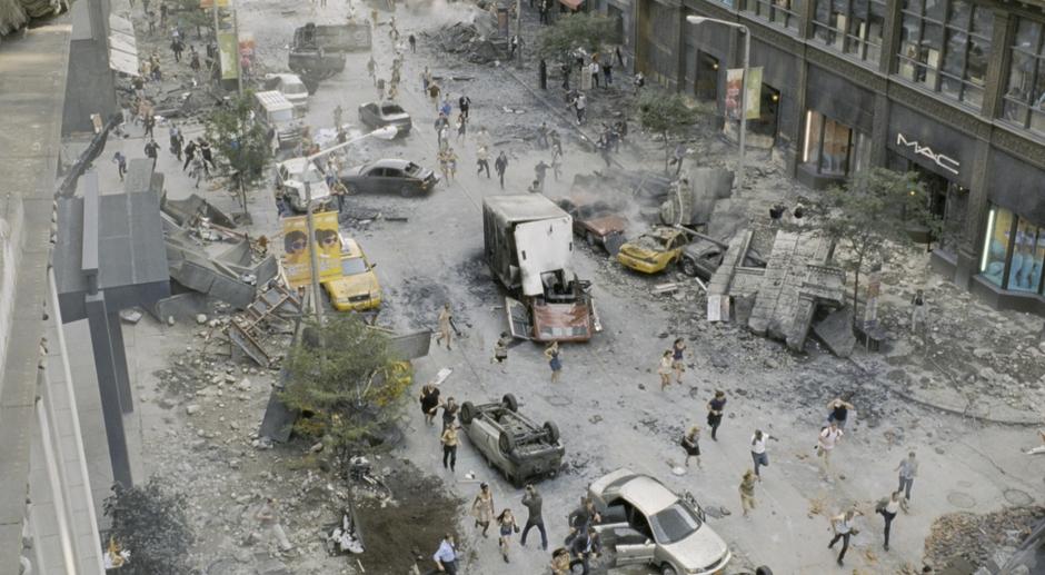 Civilians run through what remains of the cars in the street. Shot looking south down East 9th Street.