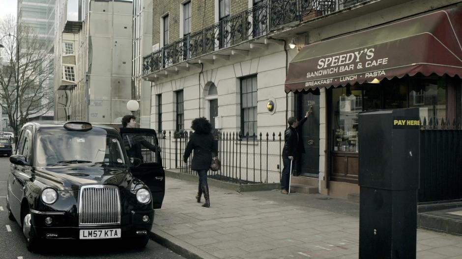 Watson knocks on the door of the flat while Sherlock gets out of a taxi.