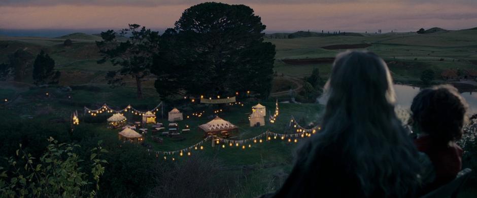 Gandalf and Bilbo smoke pipes while looking down on the party preparations.