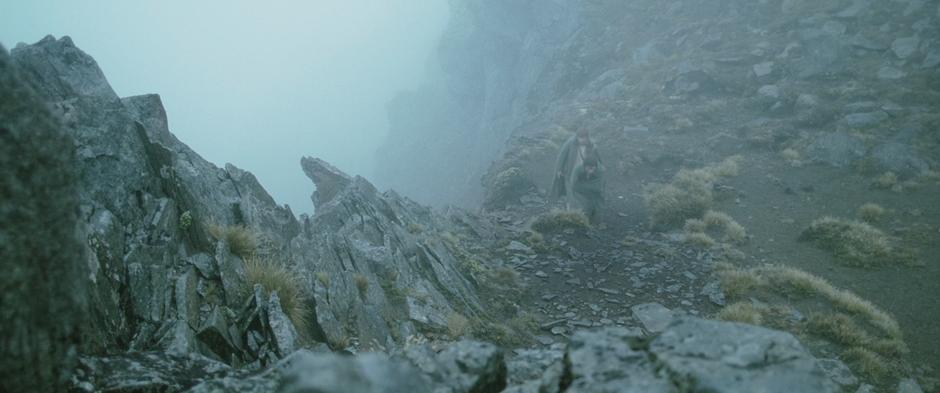 Frodo and Sam walk along the edge of a cliff in the fog.