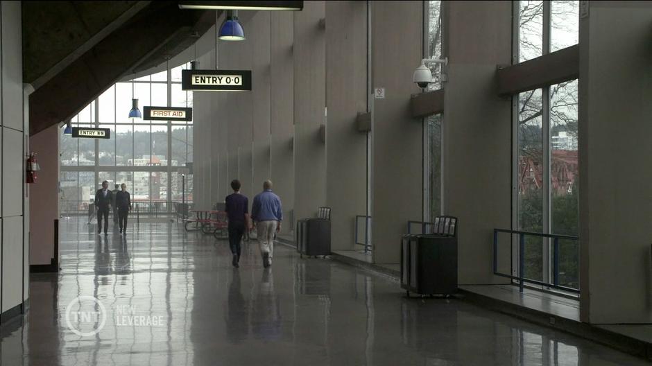 Nate and Parker discuss the heist while walking through the lobby during the game.