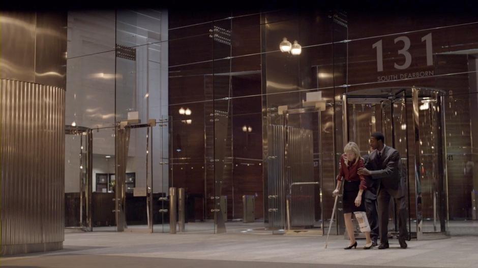 Hardison and Eliot help Parker out of the building's lobby.