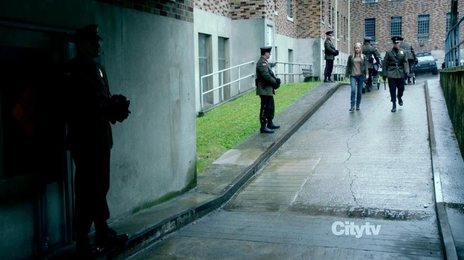 Etta walks down the ramp in front of the building and talks with one of the loyalists officers.