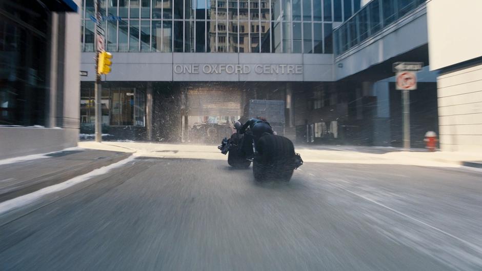 Selina follows the bomb truck and a tumbler under an overhang.