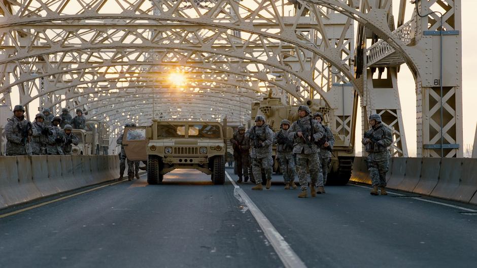 Troops and tanks from the National Guard yell across to Bane's men.