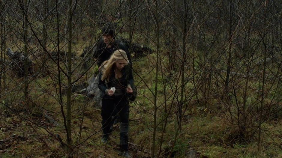 Clarke and Bellamy walk through some small trees to where the bunker should be.