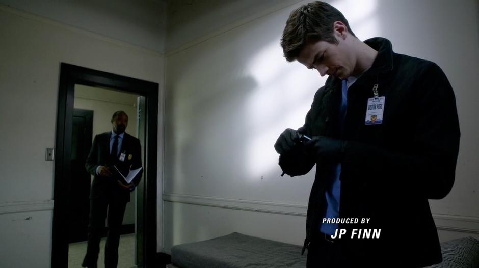 Barry takes photos of evidence in the cell while Joe goes over the case file.