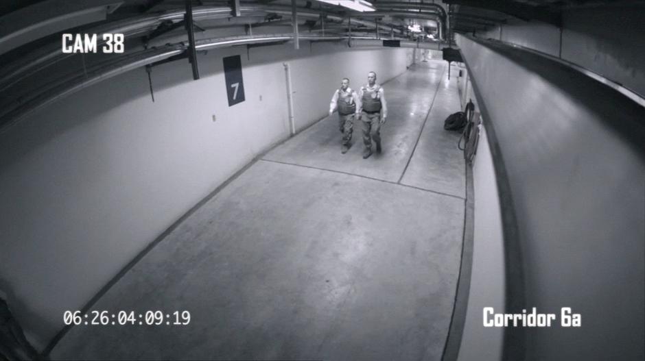 A security camera views two guards walking down a hallway.