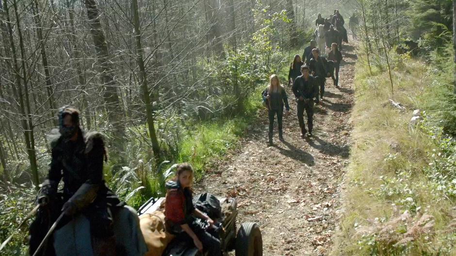 Raven rides with Finn's body on the cart while Clarke, Bellamy, and the others follow.