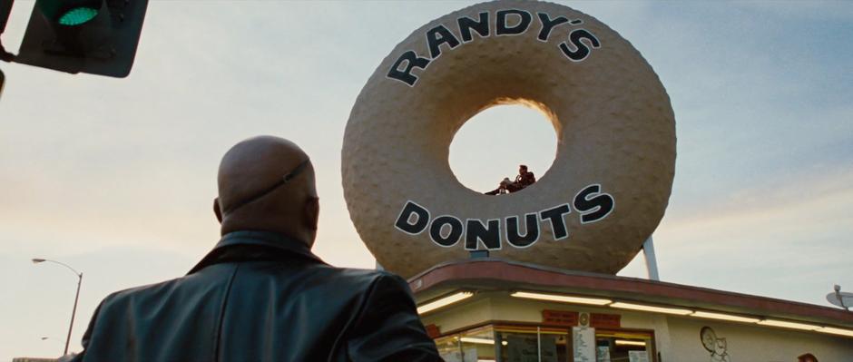 Nick Fury looks up at Tony Stark who is sitting in a donut.