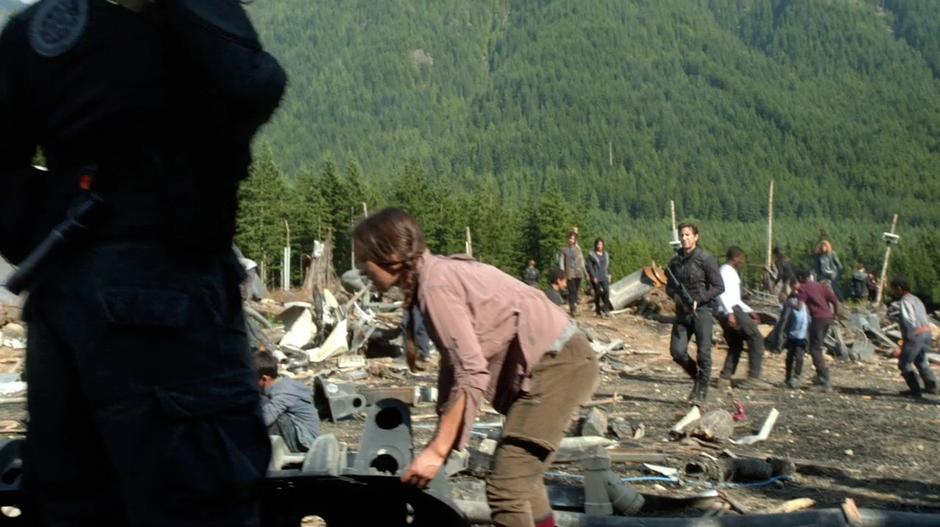 Marcus walks across the camp while survivors clear up debris.