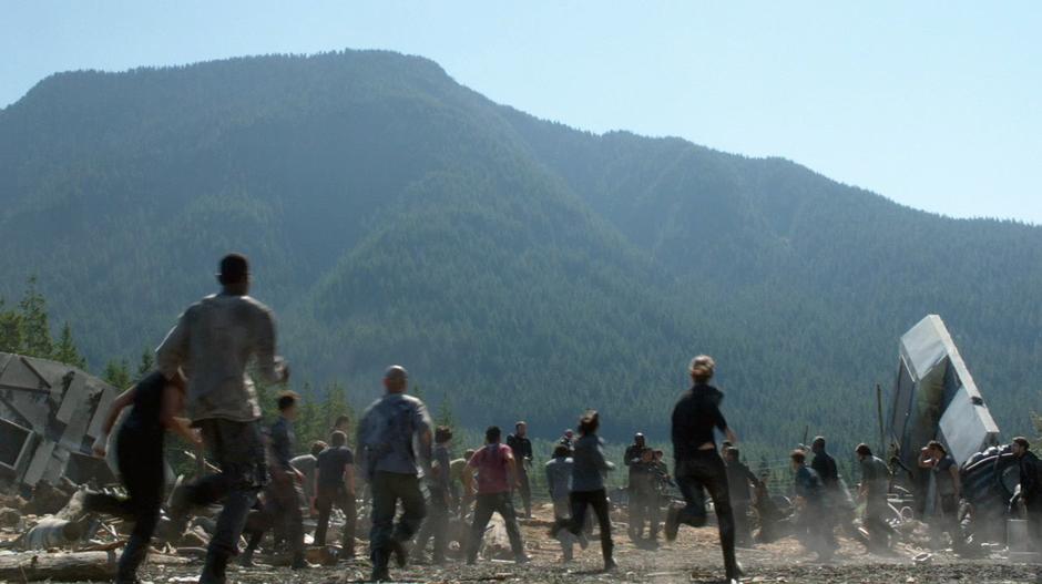 Survivors in the camp run to surround a grounder prisoner who is being brought in by a patrol.