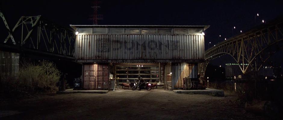 Sam approaches his container house on motorcycle.