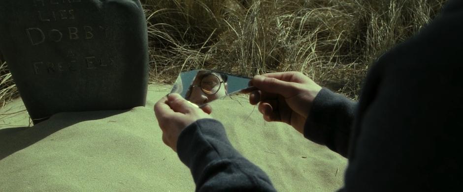 Harry looks at himself in a mirror while kneeling beside Dobby's grave.