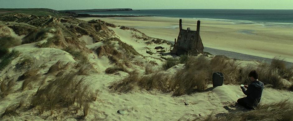 Harry kneels over Dobby's grave in a wide shot with Shell Cottage in the background.