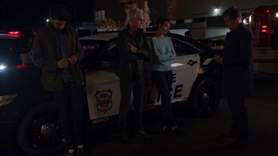 Ravi, Blaine, and Peyton are interviewed by a detective while leaning against a police cruiser out front of the office.