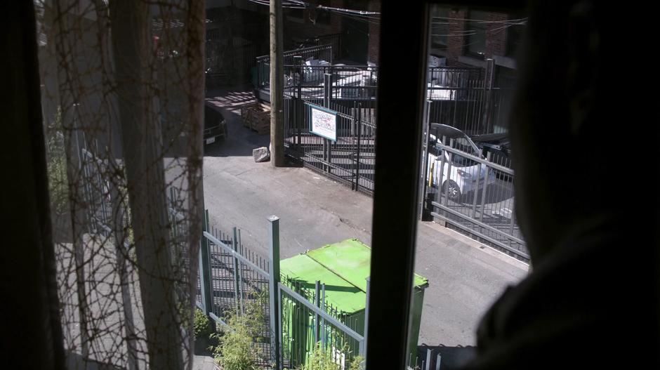 Clive looks down into the alley from the window of the apartment.