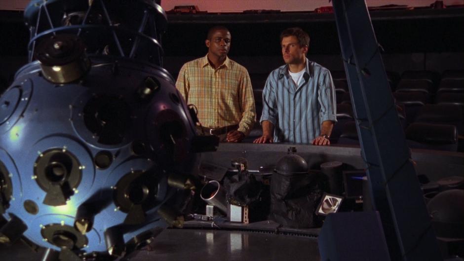 Gus and Shawn watch in the planetarium while Hugo gives his press conference.