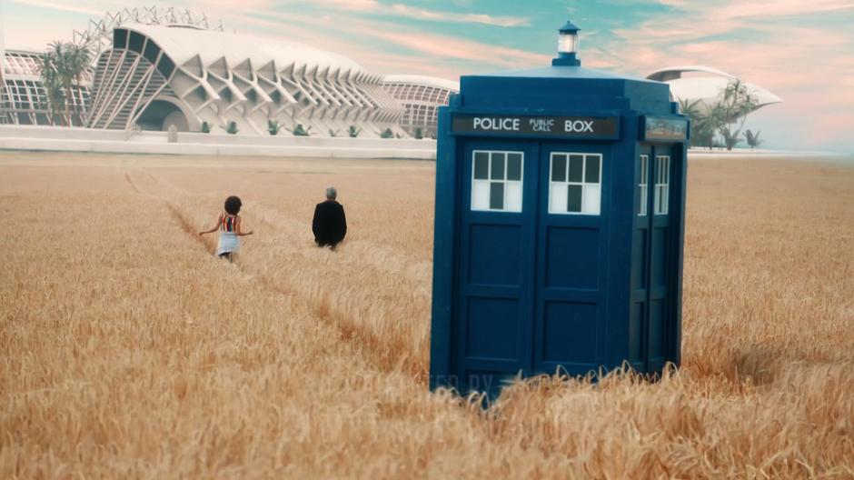 Bill and the Doctor walk through the wheat away from the TARDIS towards the colony.