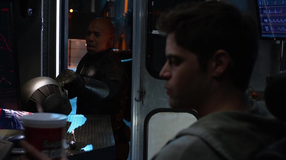 James puts his helmet down in the van while Winn sits at the desk.