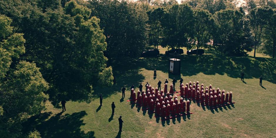 The last of the handmaids setting into their places in front of the stage while the guards stand around them.