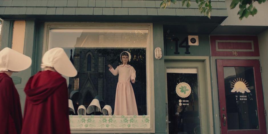 Ofglen and Offred approach the window of a dress shop.