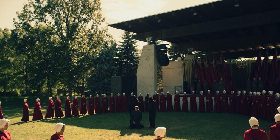 The two guards setting the rapist into the assembling circle of handmaids in front of the stage.