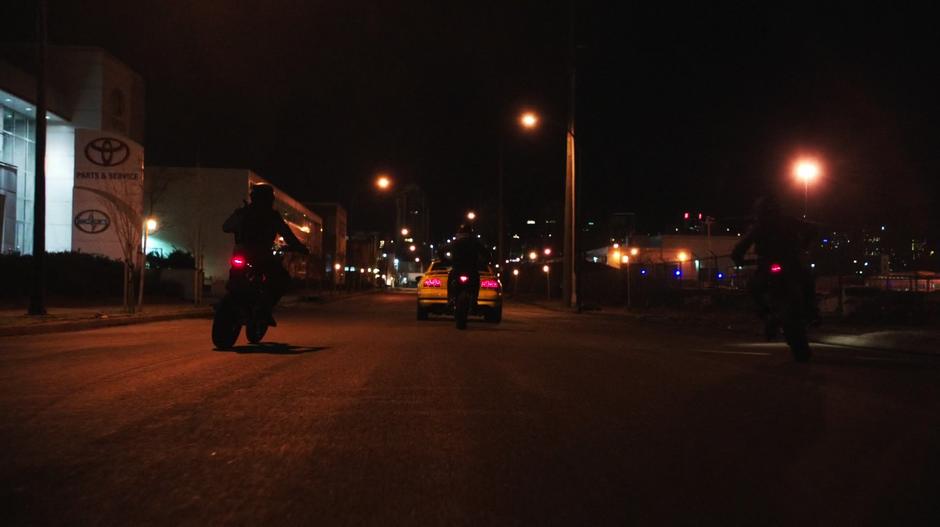 Three mercenaries on motorcycles follow the A.R.G.U.S. agent down the road.