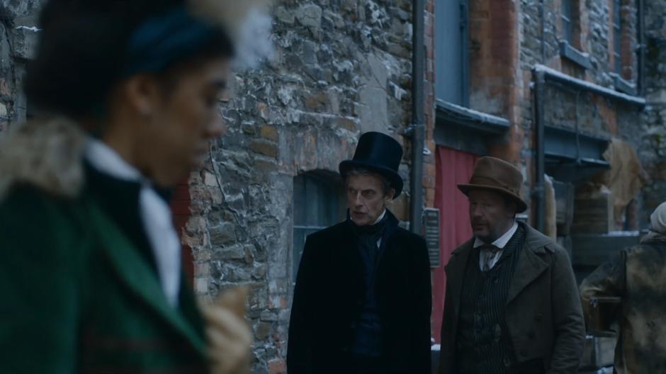 Bill examines the mud bricks in the foreground while the Doctor slyly tries to get information out of the foreman.