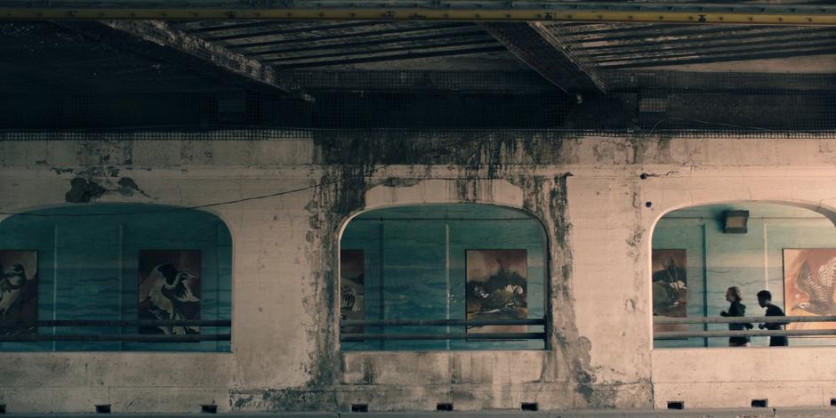 June and Moira jog beneath an underpass past a series of public artworks.