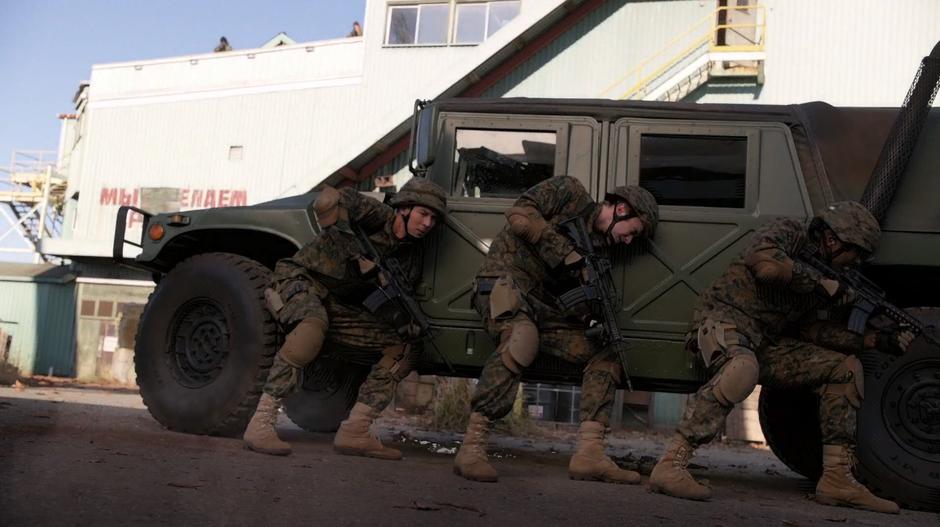 Major, Justin, and another of their team members hide behind a Humvee while two of the militants fire at them from the rooftop.