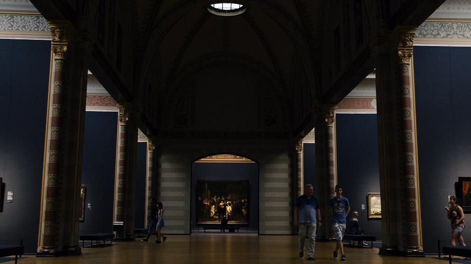 Richard Wilson Chroome sits on a bench at the end of the hall while other museum patrons mill around.