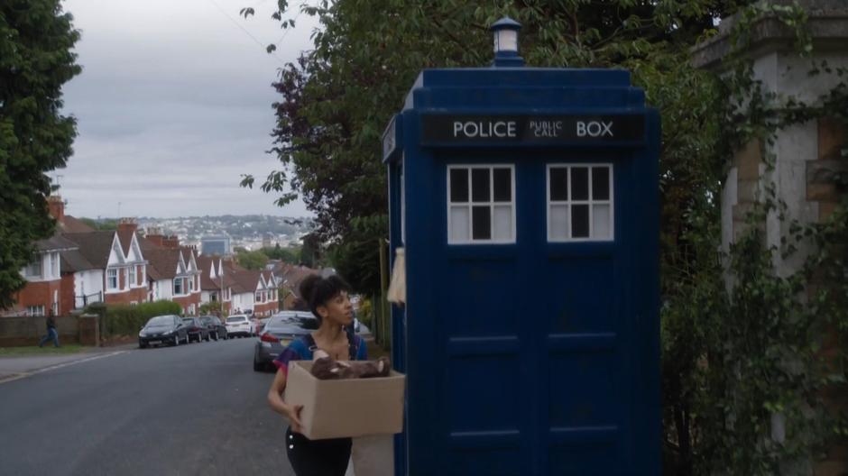 Bill exits the TARDIS which is parked on the street with a box of her stuff.