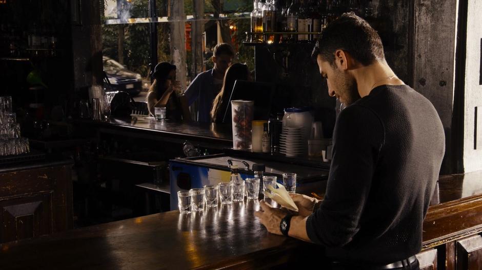 Lito pulls out the invitation to pride while eight shots are lined up on the bar in front of him.